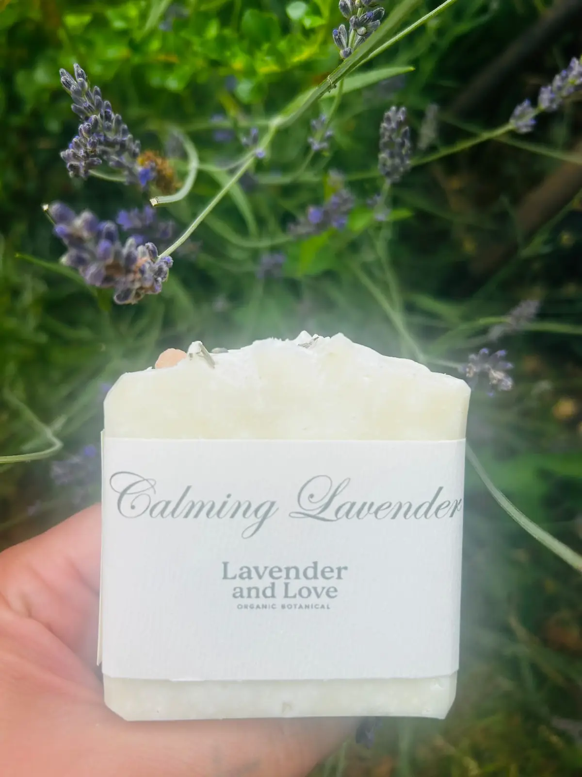 A bar of Calming Lavender soap held in front of flowering lavender