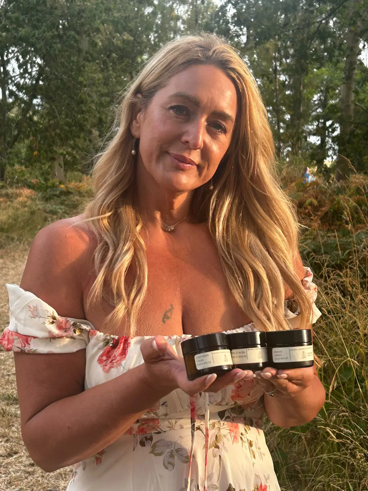 The maker of Lavender and Love holding the Lavender Calm, Wild Rose and Serene Green face balms in a woodland clearing