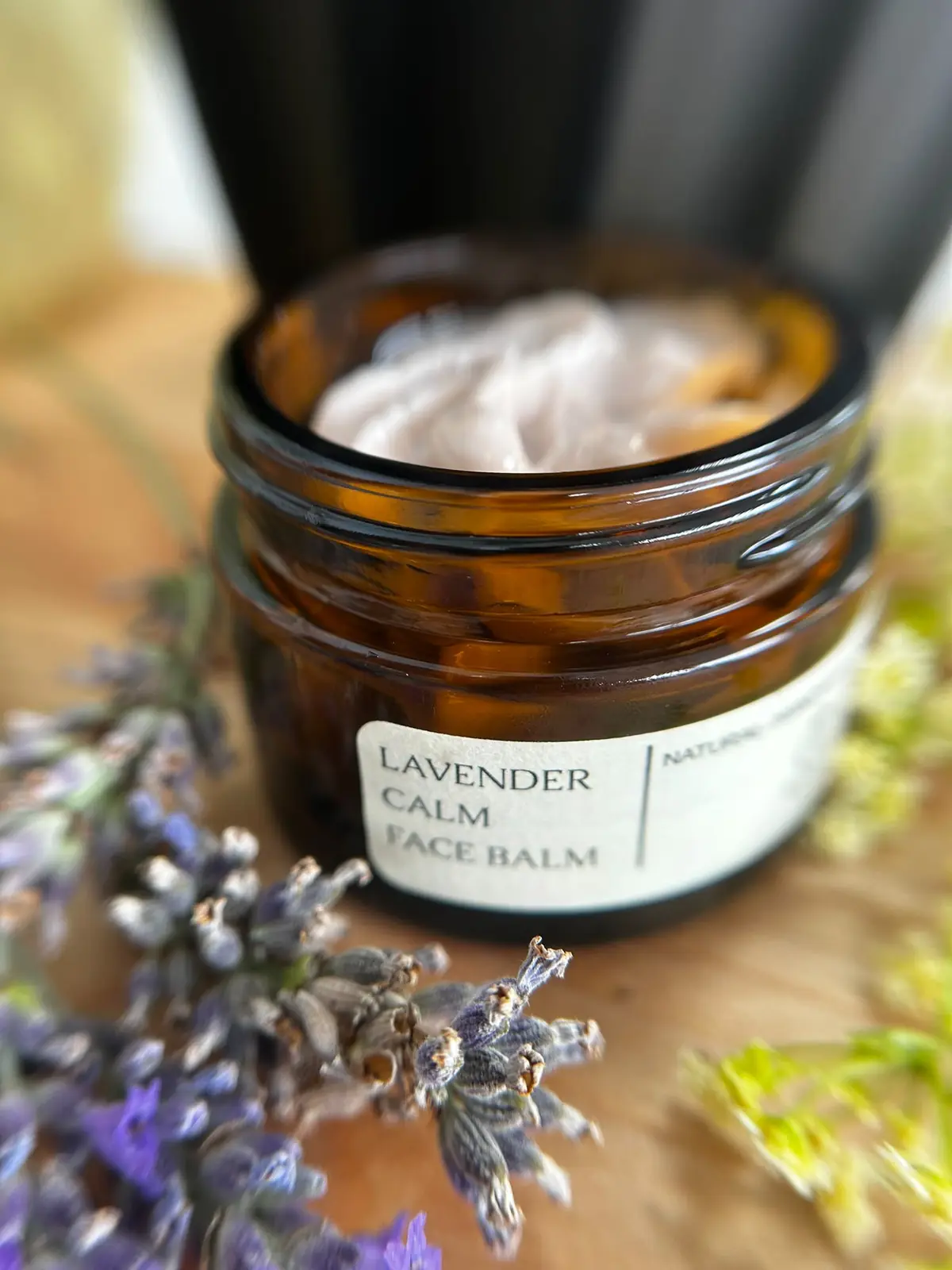 An open jar of Lavender Calm Face Balm beside sprigs of lavender
