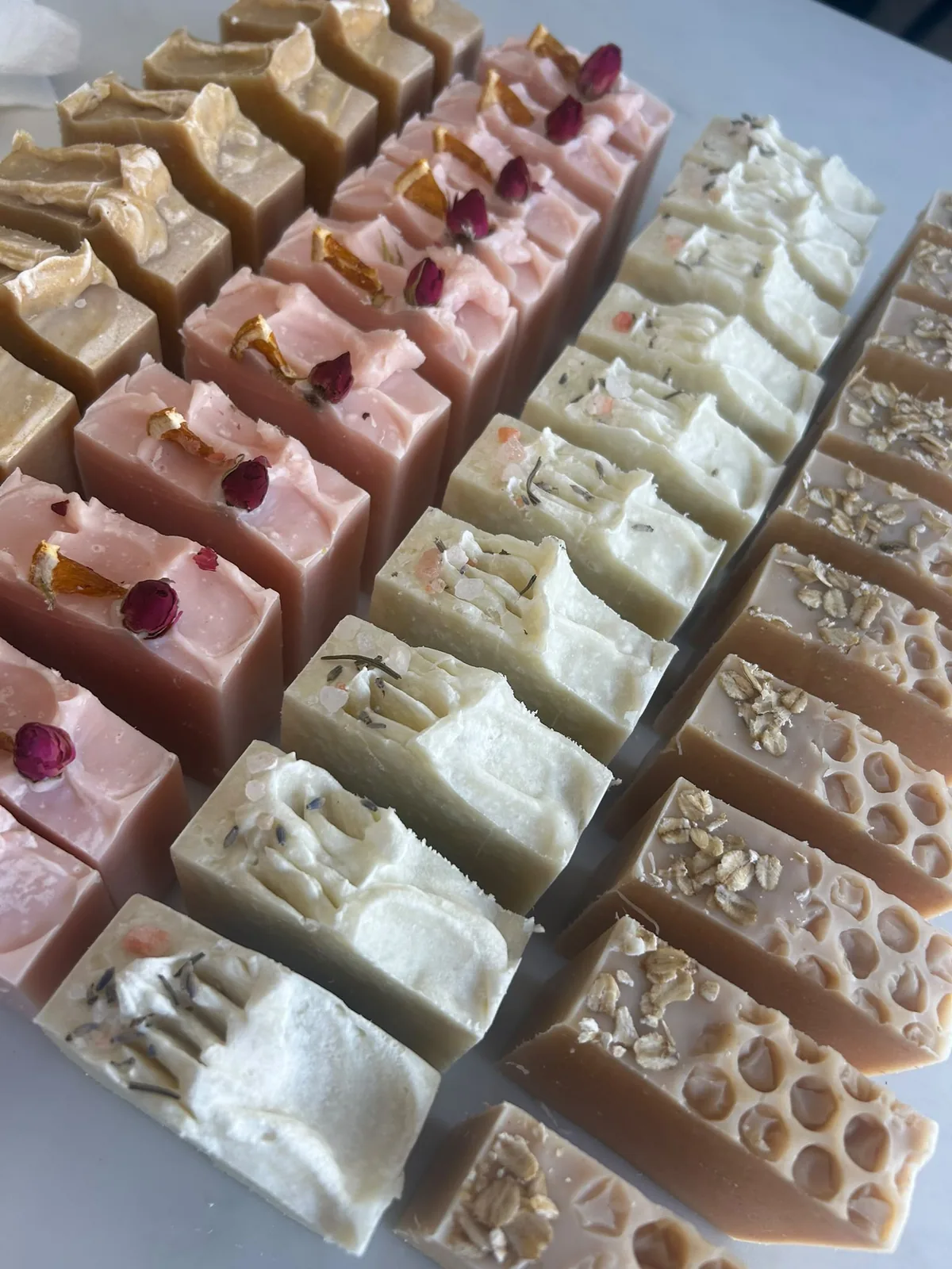 Rows of handmade soap bars: rose with dried orange and rosebuds, lavender with pink salt, oat and honeycomb, and golden bars