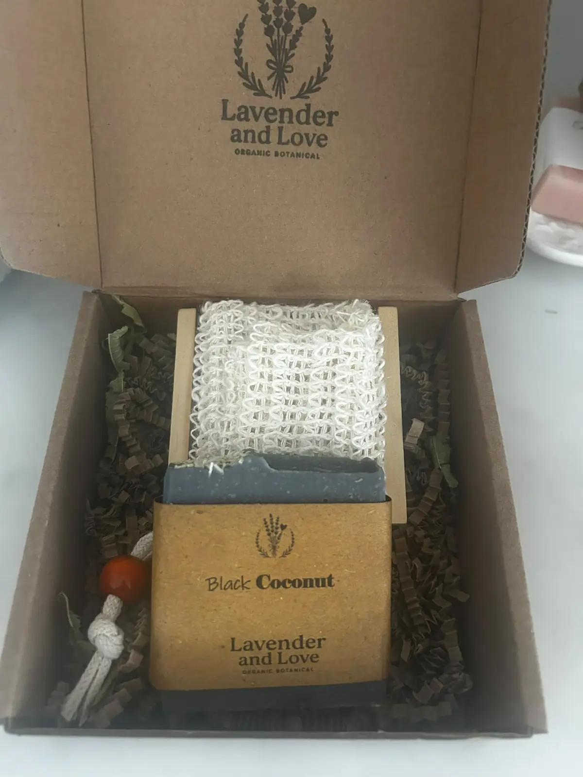 A Black Coconut soap on a soap saver bag and wooden rack, in a kraft box printed with the Lavender and Love logo