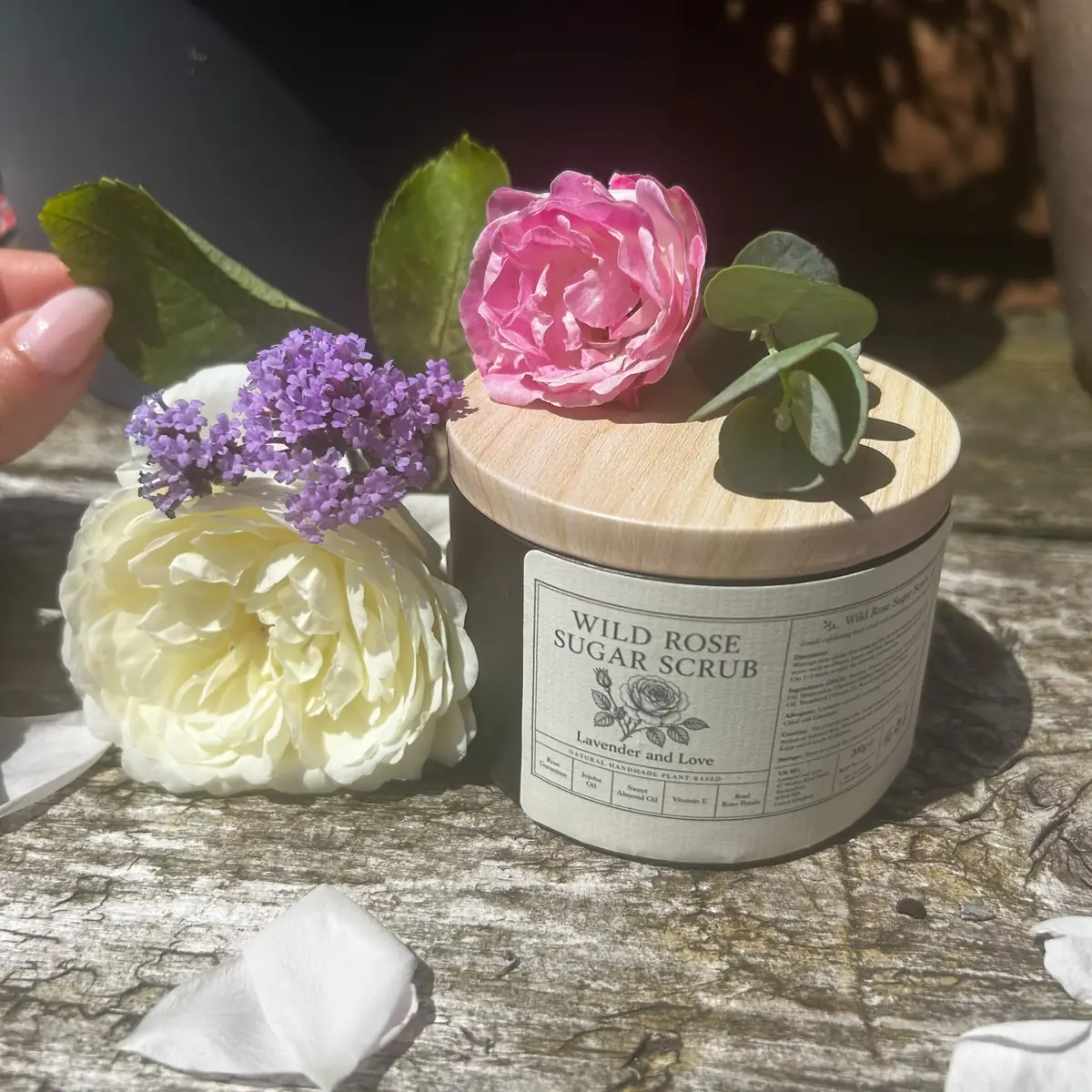Wild Rose Sugar Scrub with a wooden lid, topped with a pink rose and eucalyptus