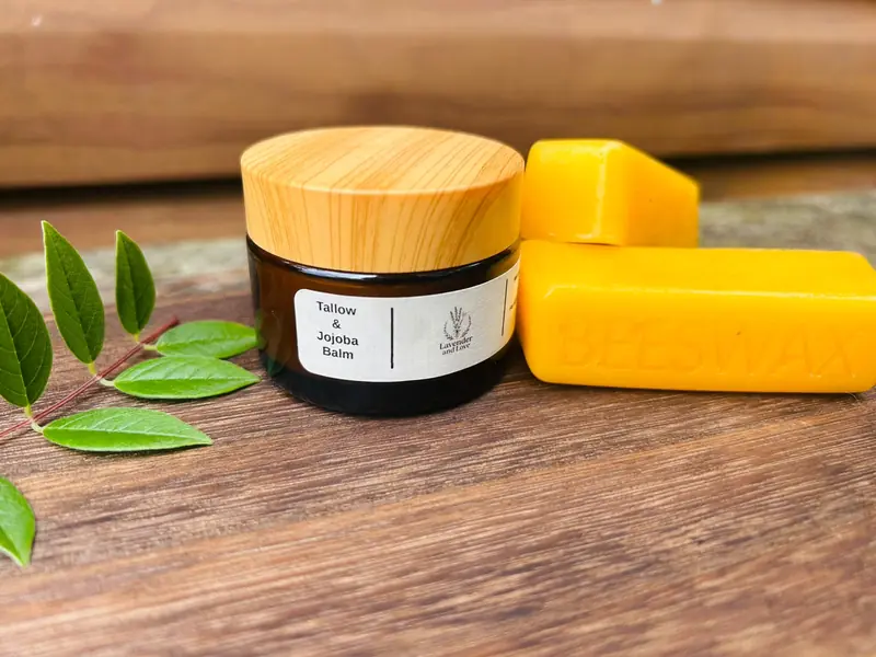 Tallow and Jojoba Balm in an amber jar with a wooden lid, beside blocks of beeswax